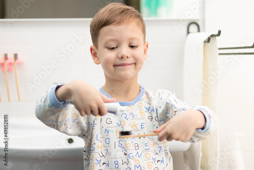 A cute seven year old boy in pajamas with a bamboo toothbrush brushes his teeth before going to bed at home in the bathroom. Selective focus. Portrait