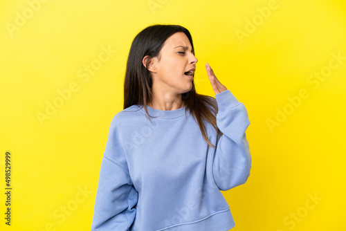 Young caucasian woman isolated on yellow background yawning and covering wide open mouth with hand © luismolinero