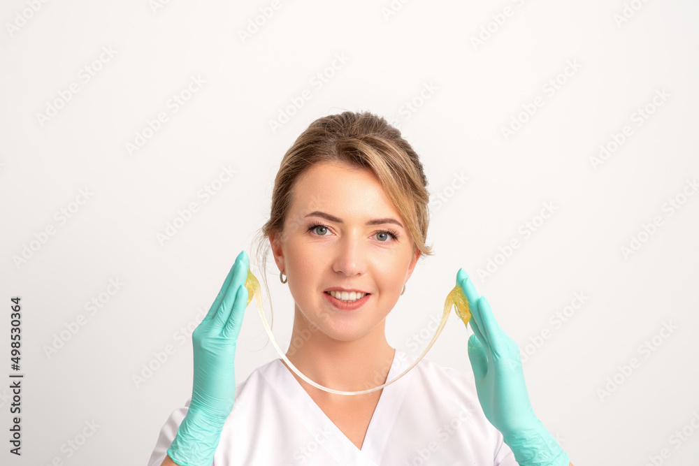 Young caucasian smiling female beautician holding wax for depilation over white background. Yellow sugar paste in hands master of depilation. Epilation concept Young caucasian smiling female beautician holding wax for depilation over white background. Yellow sugar paste in hands master of depilation. Epilation concept