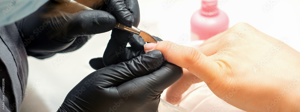 Close up professional manicurist master holding customer hand while using a cuticle pusher in a nail salon