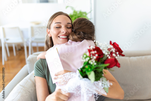 I love my you mom! Attractive young woman with little cute girl are spending time together at home, thanking for handmade card with love symbol and flowers. Happy family concept. Mother's day.