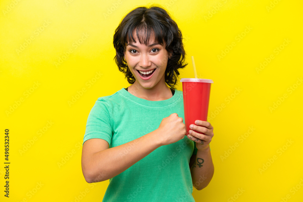 Young Argentinian woman holding a soda isolated on yellow background celebrating a victory Young Argentinian woman holding a soda isolated on yellow background celebrating a victory