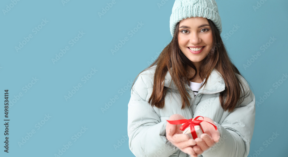 Young woman in warm gloves with gift box on blue background Young woman in warm gloves with gift box on blue background