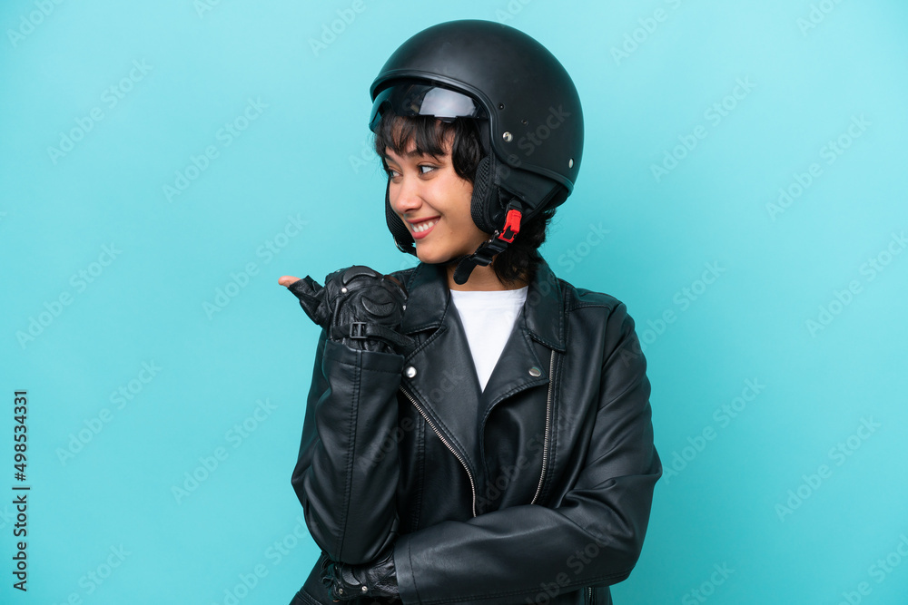 Young Argentinian woman with a motorcycle helmet isolated on blue background pointing to the side to present a product Young Argentinian woman with a motorcycle helmet isolated on blue background pointing to the side to present a product