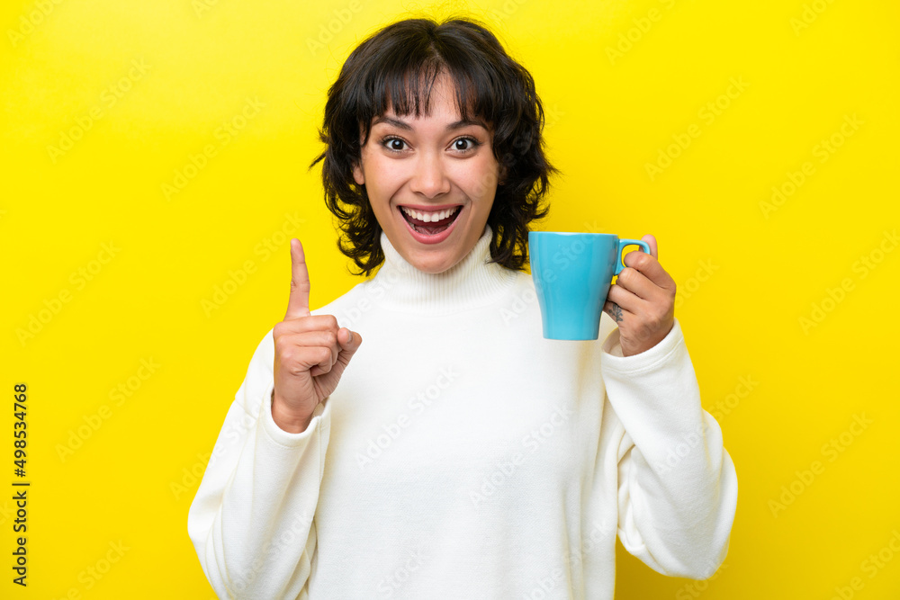 Young Argentinian woman holding cup of coffee isolated on yellow background pointing up a great idea Young Argentinian woman holding cup of coffee isolated on yellow background pointing up a great idea