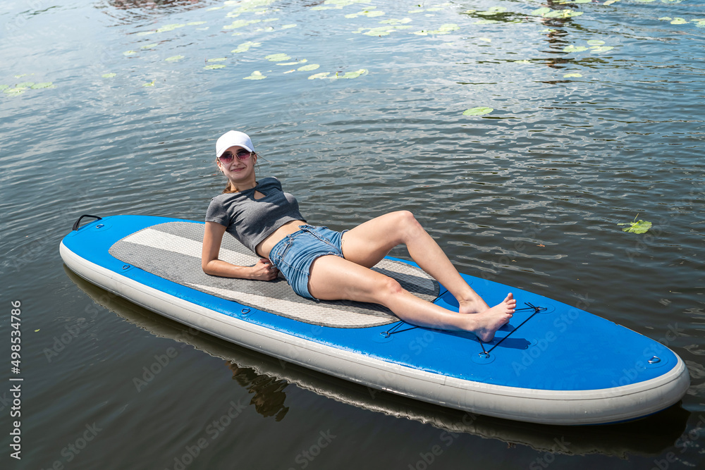 Fototapeta premium pretty young slim female model lying on sup board at sunny morning at ocean beach