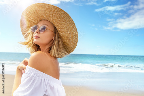 Portrait of blonde caucasian girl in summer straw hat and fashionable sunglasses walking, relaxing at the beach. Vacation vibe. Sunny day. Travel, tourism concept.