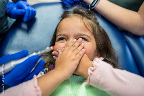 on the dental chair lies a little girl who is about to open her mouth to the dentist.