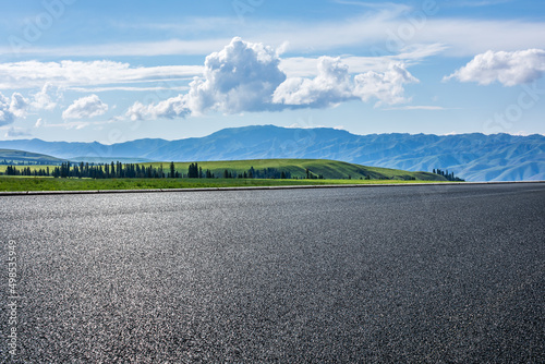 Empty asphalt road and green grassland and mountain under blue sky © ABCDstock