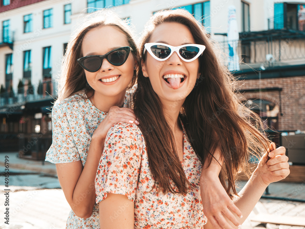 Two young beautiful smiling hipster female in trendy summer dress clothes.Sexy carefree women posing on the street background. Positive models Two young beautiful smiling hipster female in trendy summer dress clothes.Sexy carefree women posing on the street background. Positive models