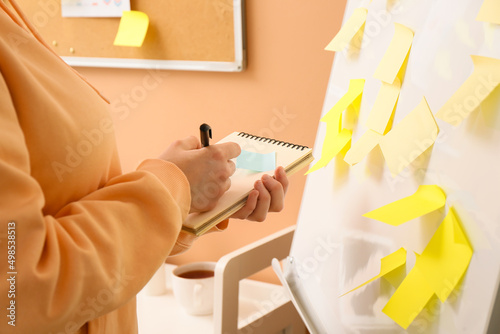 Woman writing on notebook near flipchart with sticky notes in room