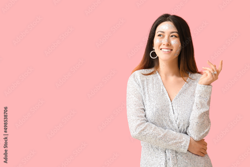 Smiling Asian woman with glitter makeup and stylish jewelry on pink background