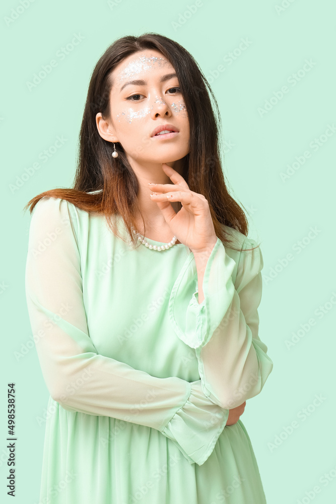 Young Asian woman with glitter makeup touching chin on color background Young Asian woman with glitter makeup touching chin on color background