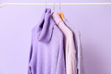 Rack with lilac sweaters on color background