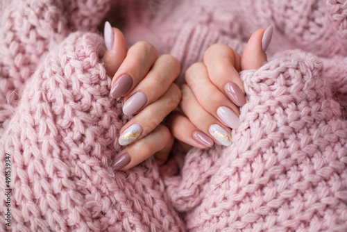 Women's hands with a beautiful  oval manicure in a warm pink knitted sweater. Winter trend, polish beige nails with gel polish, shellac. Copy space.