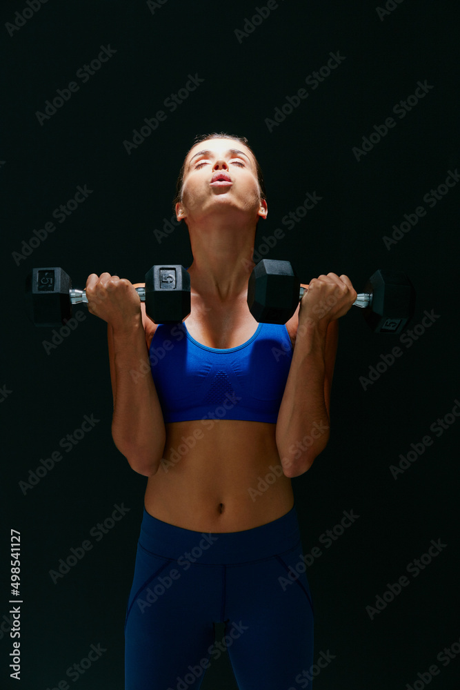 Hustle for your muscle. Studio shot of a fit young woman working out with weights against a dark background. Hustle for your muscle. Studio shot of a fit young woman working out with weights against a dark background.