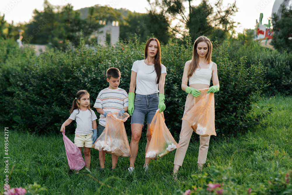 Fototapeta premium A group of adults and children together at sunset is engaged in garbage collection in the park. Environmental care, waste recycling. Sorting garbage.