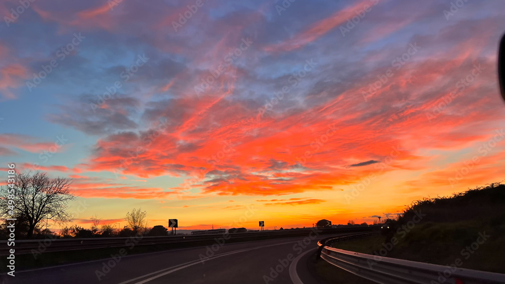 Tramonto con luci rosse e arancioni su una curva di un autostrada italiana