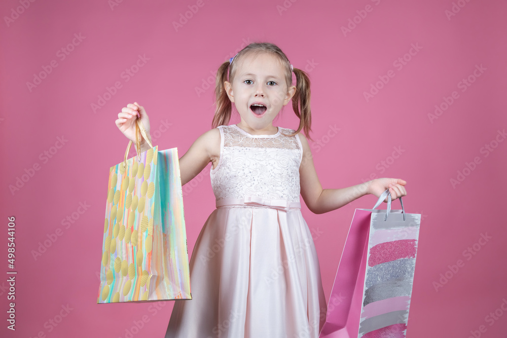 Funny girl in a party dress with shopping bags isolated over pink background