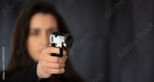 Woman with a gun point to camera. Female secret police agent, killer or spy, copy space