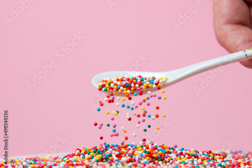 Confectionery sprinkles are sprinkled from a spoon on a pink background. Topping for desserts and pastries. small caramel balls photo