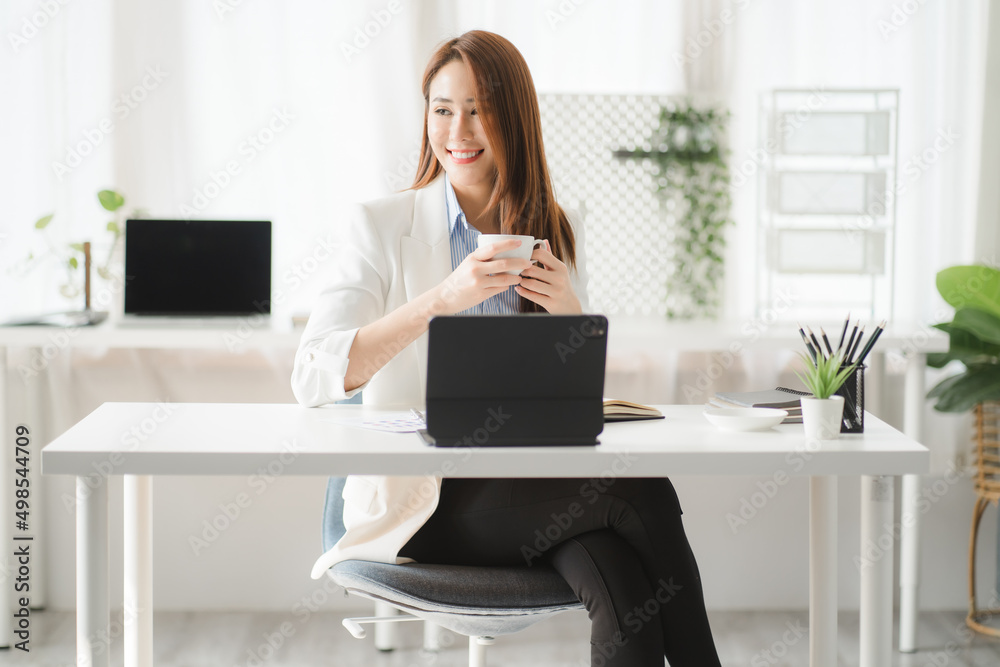 Portraits of beautiful smiling Asian women relax using laptop computer technology while sitting on their desks and using their creativity to work, work from home concept.