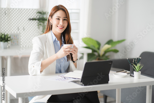 Portraits of beautiful smiling Asian women relax using laptop computer technology while sitting on their desks and using their creativity to work, work from home concept.