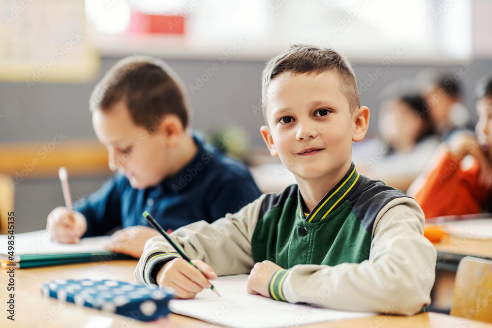 A clever boy writes schoolwork on class and smiling at the camera. A clever boy writes schoolwork on class and smiling at the camera.