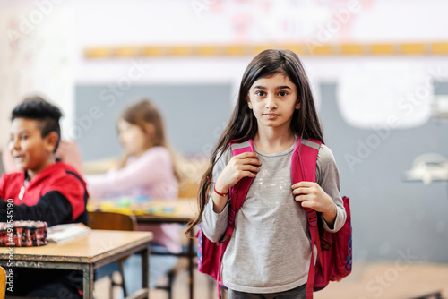 A small Indian schoolgirl with backpack posing in the classroom.