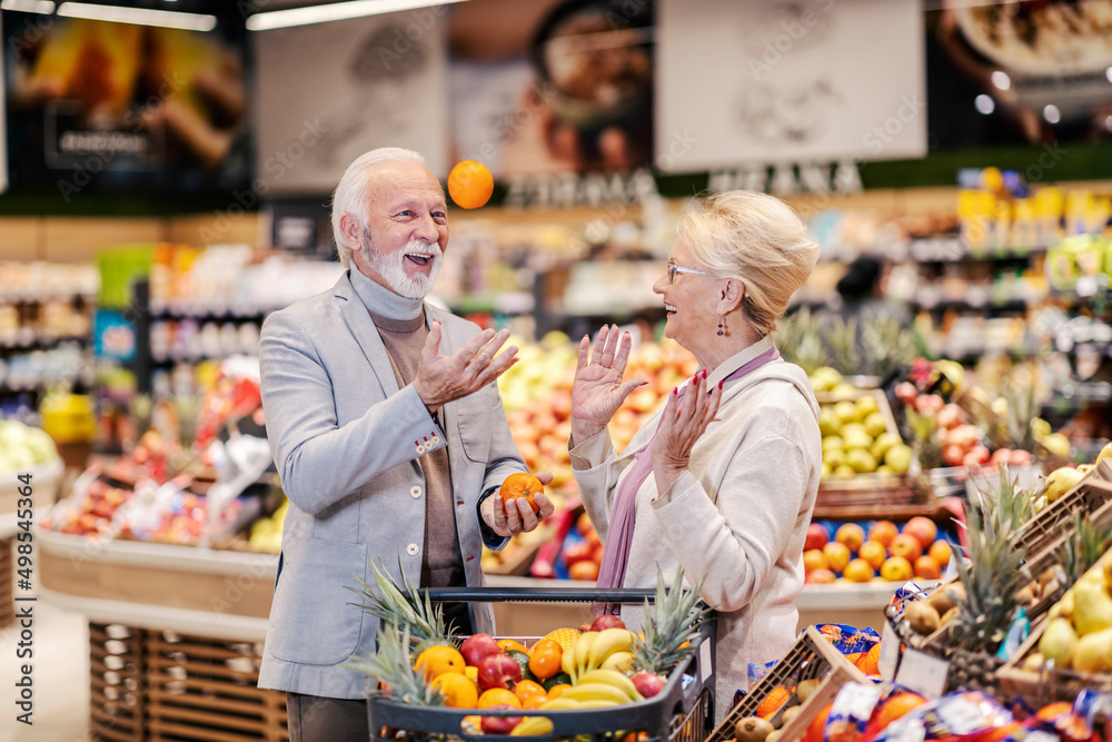 A senior couple at supermarket shopping fruits and laughing on low prices.