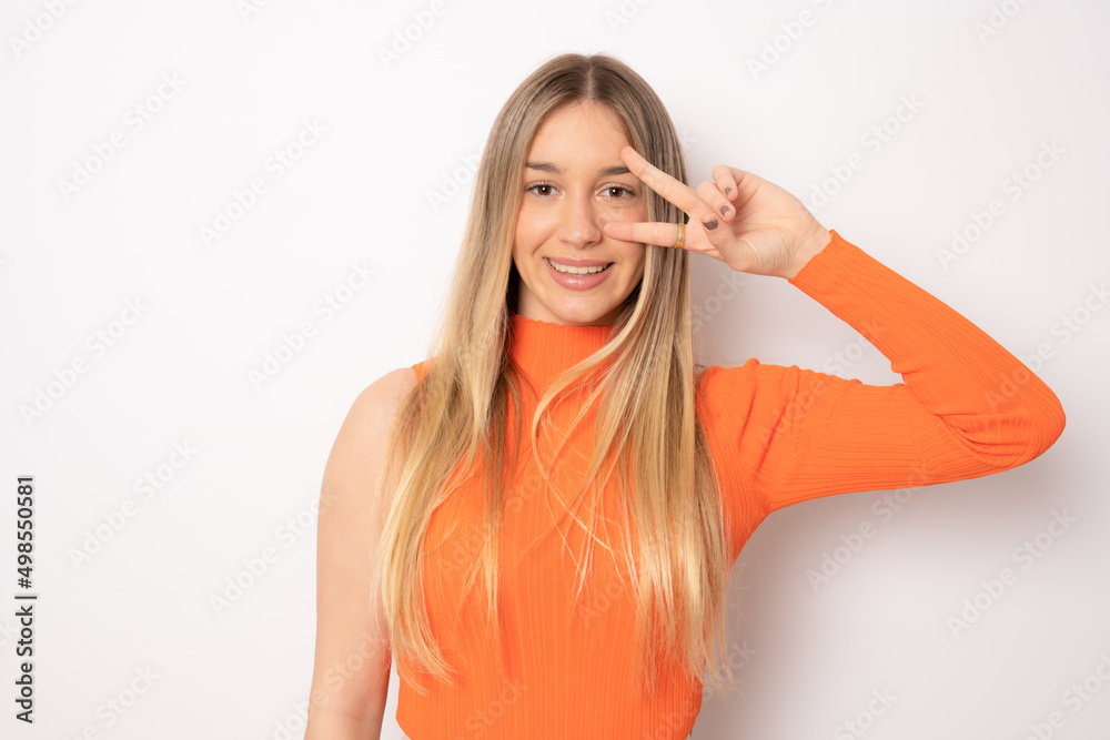 Young beautiful blonde woman wearing casual clothing over isolated white background smiling with happy face winking at the camera doing victory sign. Number two.