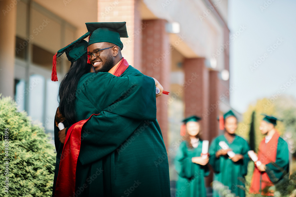 Happy black graduate and his female classmate congratulate each other on their graduation day.