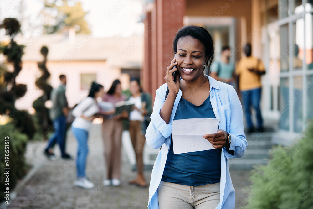 Happy black college student reads her exam result while making phone call over cell phone at campus.