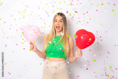 Portrait of a happy beautiful young woman standing under confetti rain and celebrating isolated over white background