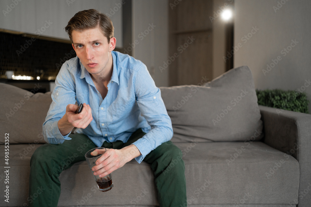 Weekend entertainment and pastime concept. adult european man watching an interesting movie indoors, holding a remote control, sitting cross-legged,