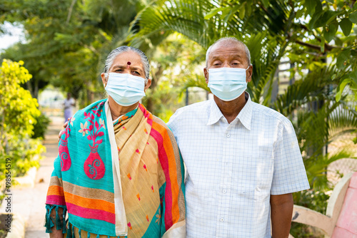 Senior couples with medical face mask during morning walk at park - concept of covid-19 coronavirus protection, healthcare and safety.