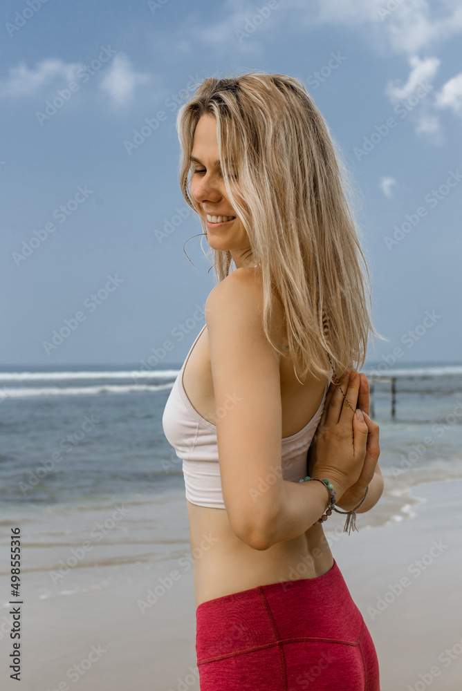 Vertical photo of Young yogi woman practicing yoga, standing in sea with Namaste behind the back, working out wearing black swimsuit. Vertical photo of Young yogi woman practicing yoga, standing in sea with Namaste behind the back, working out wearing black swimsuit.