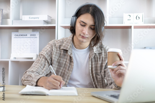 Asian man taking notes in notebook while studying online in laptop at home, Video chat, Online communication , Stay home, New normal, Distance learning, Social distancing, Learn online.