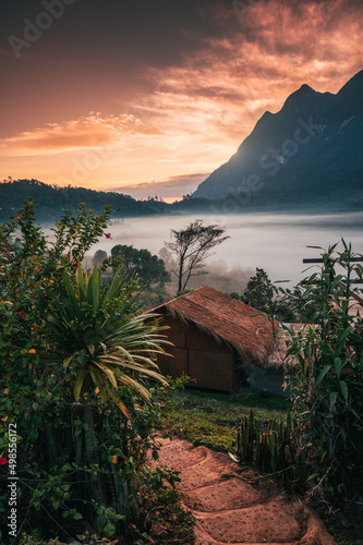 View of wooden hut with colorful sky in tropical rainforest and foggy flowing in the valley at countryside