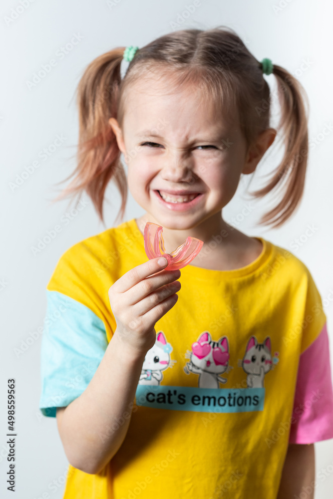 Cute little girl with blond hair is holding a pink dental myofunctional trainer Cute little girl with blond hair is holding a pink dental myofunctional trainer