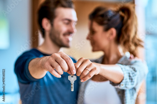The keys to our new home. Shot of a cheerful young couple holding a key together to their new home while standing inside during the day.