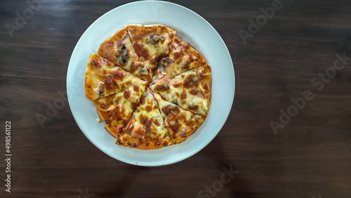 Crispy thin crust pizza with mushroom and sausage on white plate on wooden table