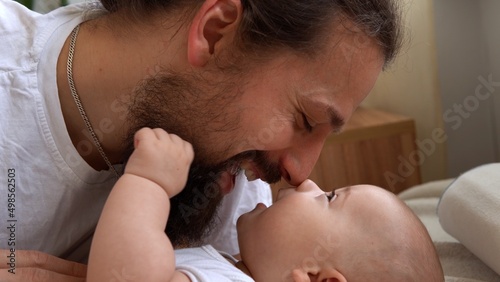 Authentic Young Bearded Man Holding Newborn Baby. Dad And Child Son On Bed. Close-up Portrait of Smiling Family With Infant On Hands. Happy Marriage Couple On Background. Childhood, Parenthood Concept