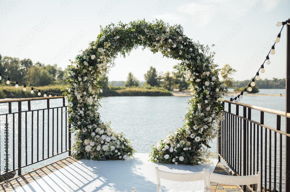 Circle wedding arch decorated with white flowers and greenery outdoors.