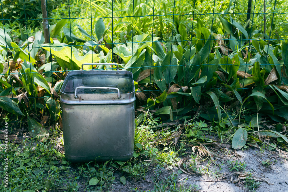 Iron square bucket with water in the garden. A square container filled with water in a flower garden Iron square bucket with water in the garden. A square container filled with water in a flower garden
