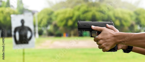 Automatic black 9mm pistol gun holding in hands of shooter and aiming to the man-target shooting paper ahead, concept for training and practising human to be body guard, vip protecting and gangsters.