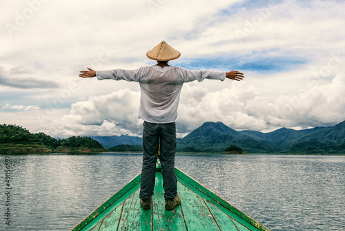 Man wearing a chinese hat standing with open hands on the edge of a boat in the Myo Gyi Dam, Myanmar photo