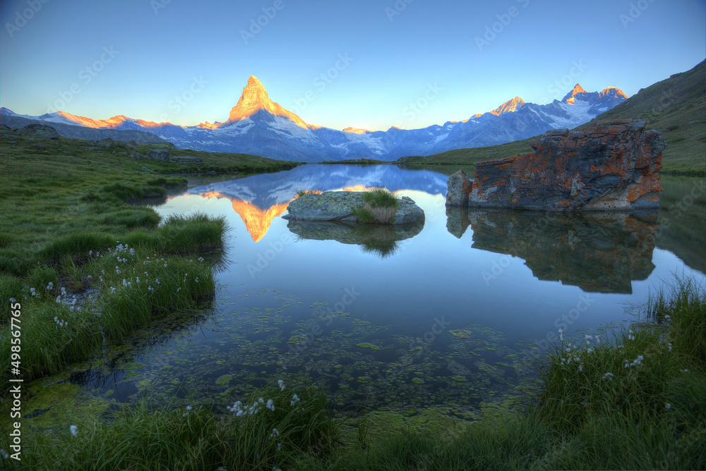Scenery of majestic Matterhorn at sunrise, with golden glow on the mountaintop and symmetric reflections in the peaceful Lake Stellisee on a beautiful summer morning, in Zermatt, Valais, Switzerland