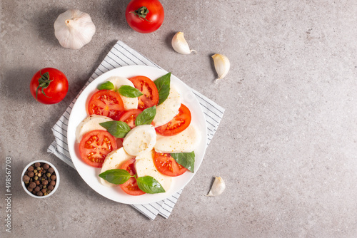Delicious Italian caprese salad with sliced mozzarella, tomatoes, basil, pesto and garlic on background.