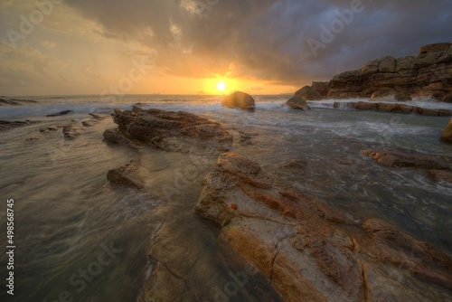 Beautiful sunrise scenery of a rocky beach on northern coast of Taiwan with golden sun rising on distant horizon & turbulent waves beating on rugged rocks under dramatic dawning sky (Long Exposure)